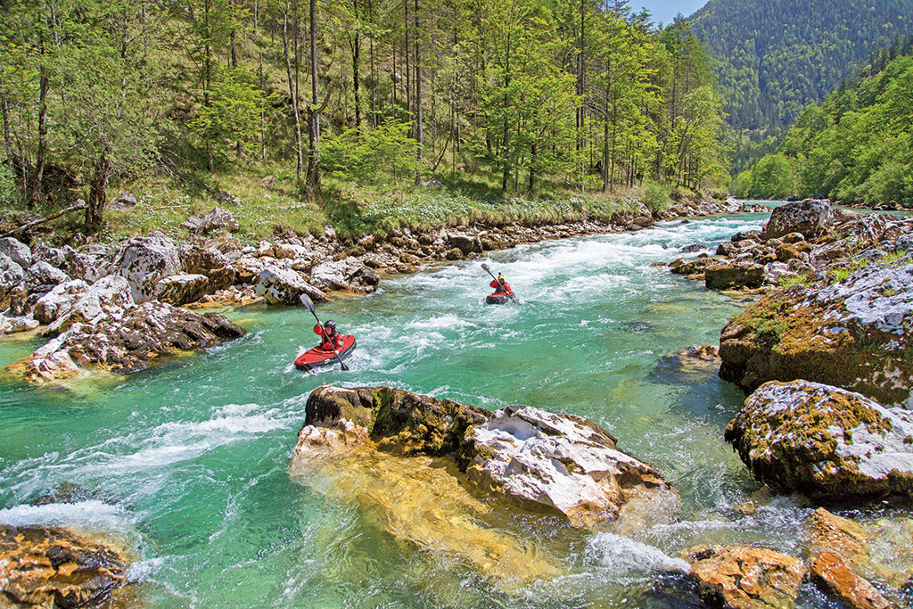 Wassersport-Zubehör für Camper: Zwei Personen fahren in roten Kajaks durch einen Fluss mit vielen Felsen