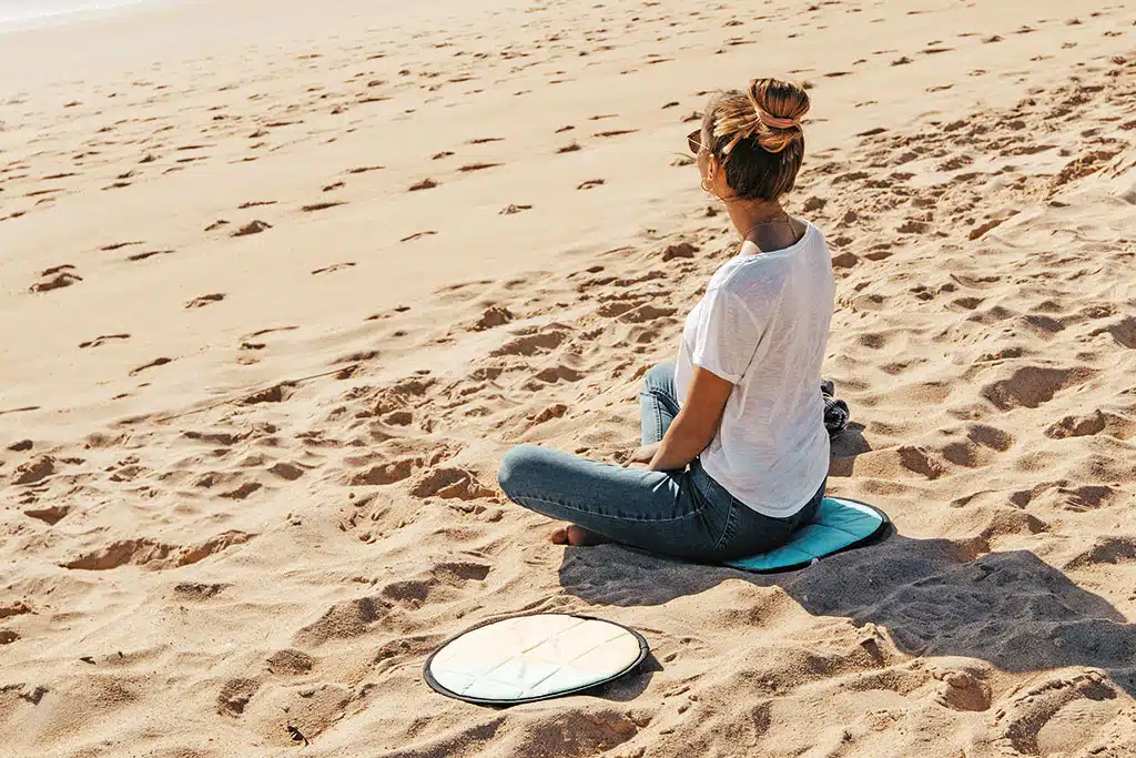 Eine Frau sitzt auf einem runden SItzkissen am Sandstrand