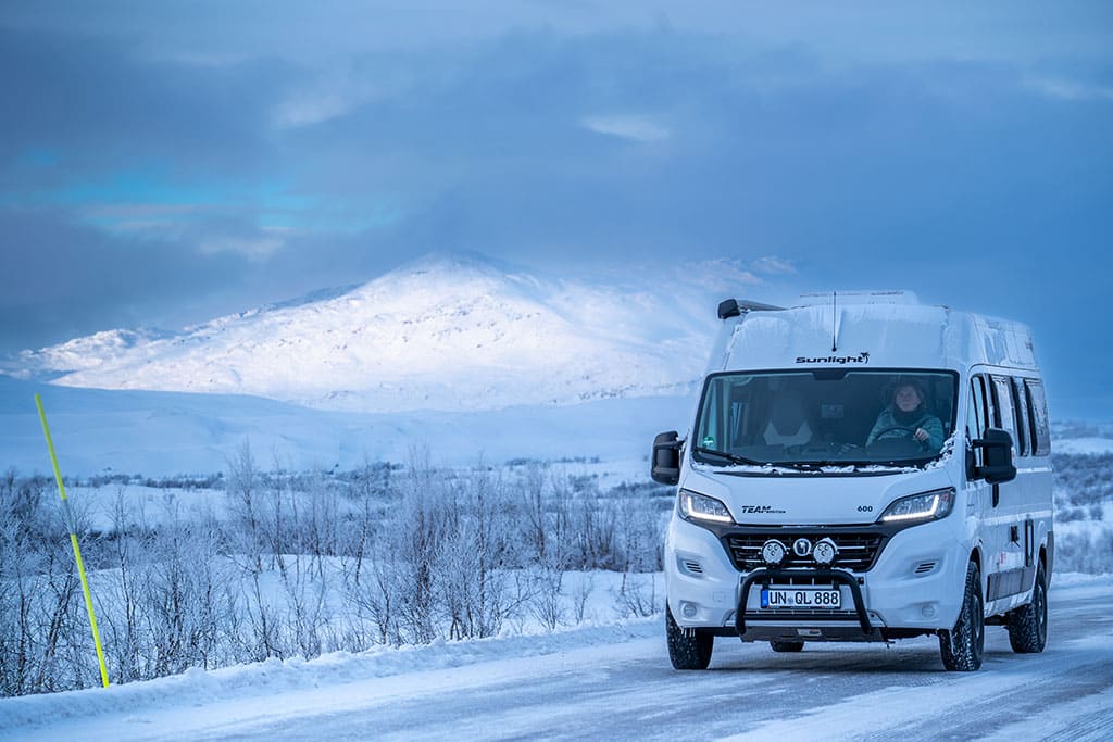 Weißer Campervan fährt durch eine weite, verschneite Landschaft