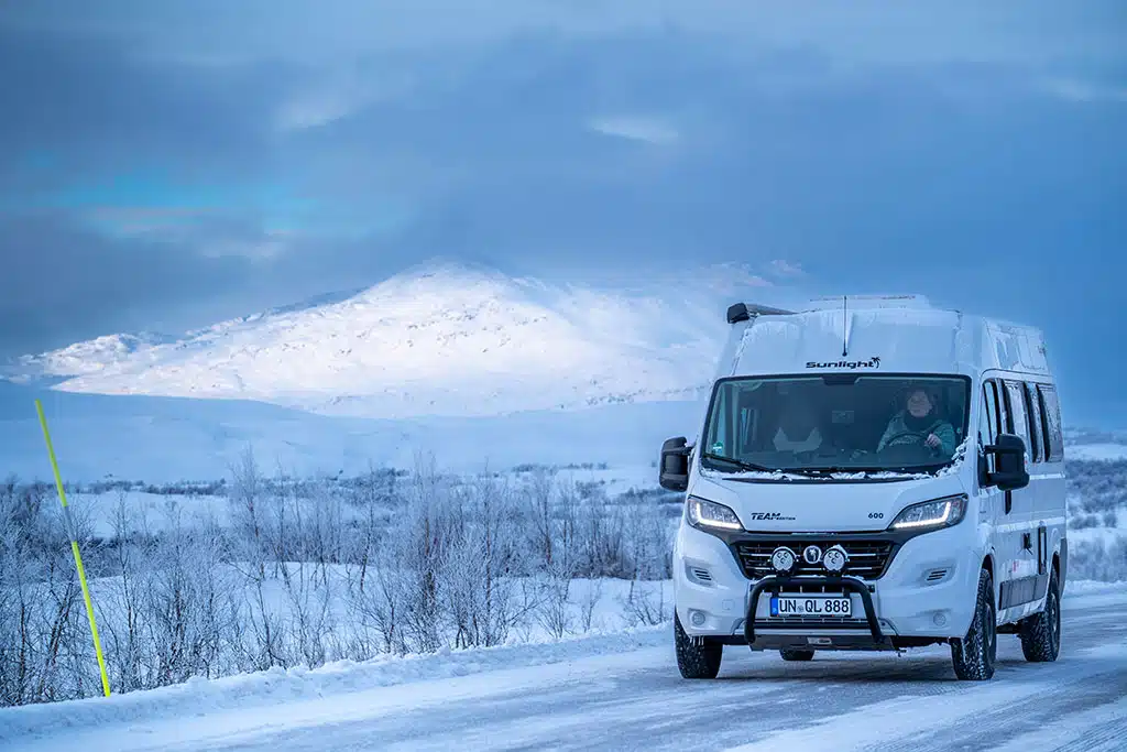 Weißer Campervan fährt durch eine weite, verschneite Landschaft