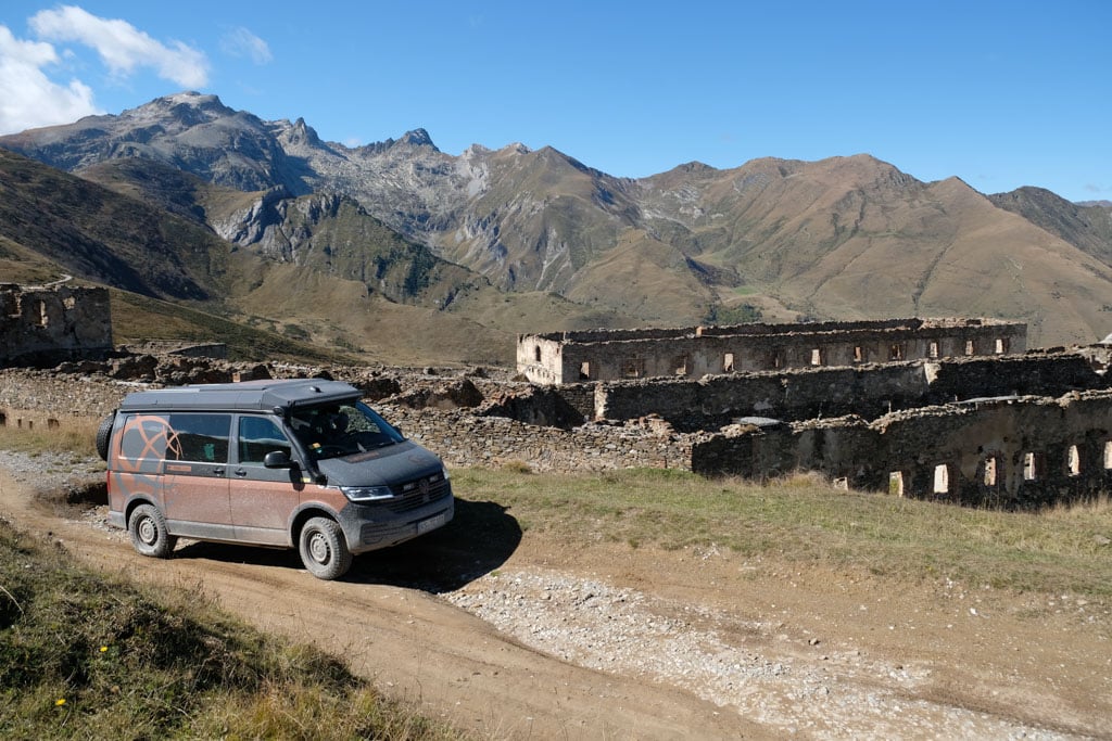 Ein Fahrzeug passiert eine alte Fort-Anlage, dahinter hohe Berge