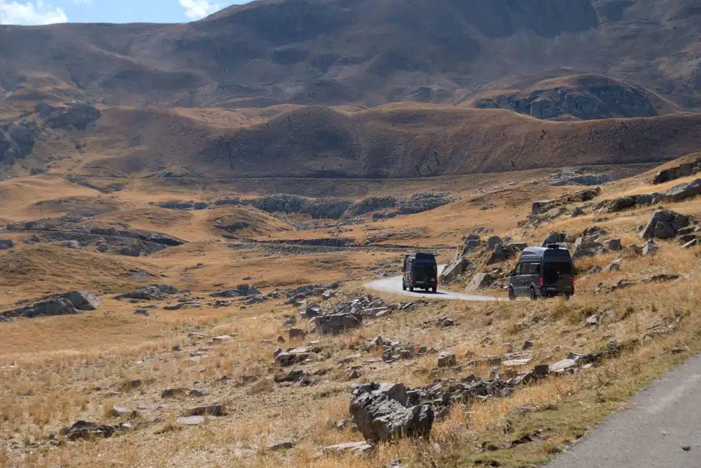 Zwei Kastenwagen auf einer gewundenen Straße durch karge Gebirgslandschaft