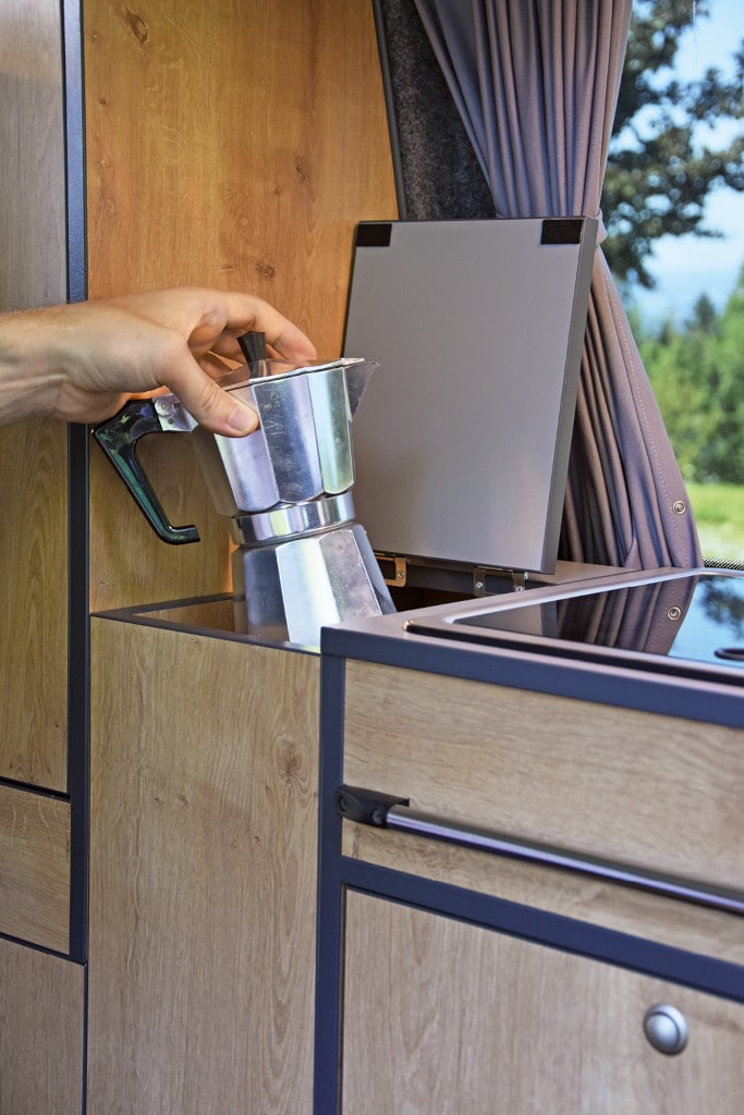 Kaffekocher wird aus in nach oben öffnender Box neben Herd gestellt