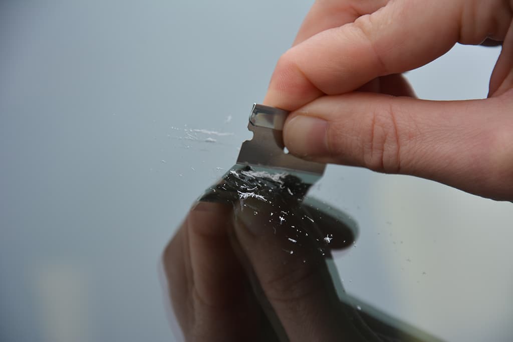 Harz wird mit Rasierklinge von einer Windschutzscheibe entfernt