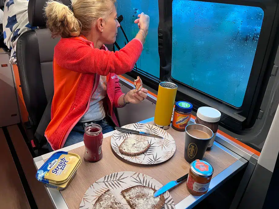 Eine Frau sitzt auf einem Autositz an einem kleinen Tisch im Campingfahrzeug und schaut aus dem Fenster