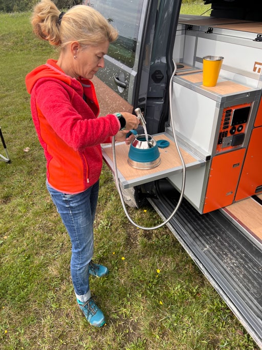 Eine Frau steht an einer kleinen Außenküche in der Schiebetür eines Campingbusses