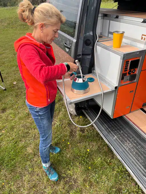 Eine Frau steht an einer kleinen Außenküche in der Schiebetür eines Campingbusses