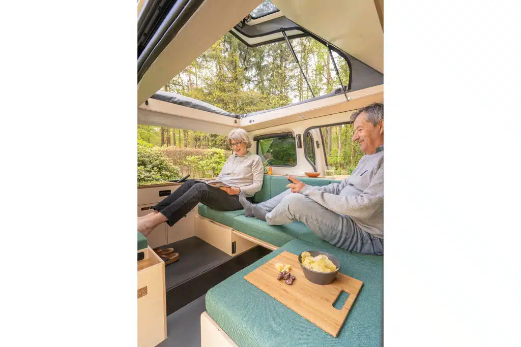 Eine Frau und ein Mann sitzen auf einer L-förmigen Lounge in einem Campingbus.