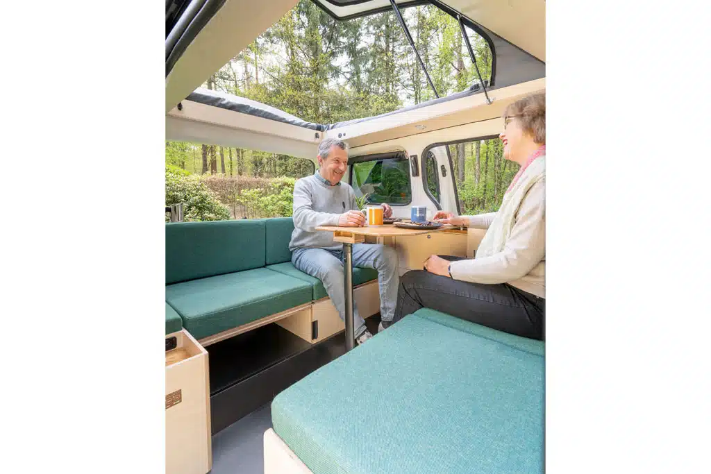 Eine Frau und ein Mann sitzen sich auf gegenüberliegenden Sitzbänken in einem Campingbus gegenüber.