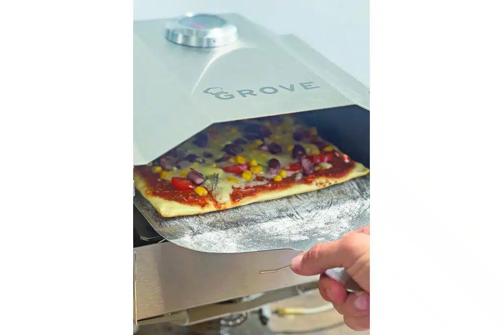 Eine rechteckige Pizza wird mit einem Edelstahlschieber aus einem Mini-Edelstahlbackofen geholt