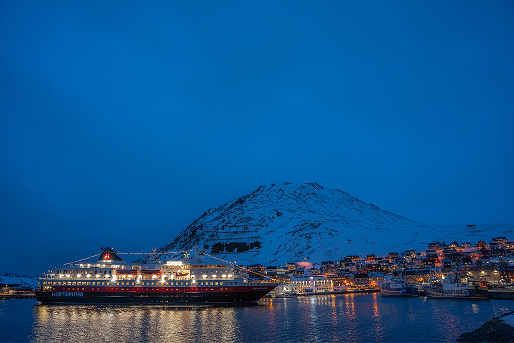 Lichter einer Hafenstadt und eines Schiffes bei Dämmerung in Skandinavien im Winter.