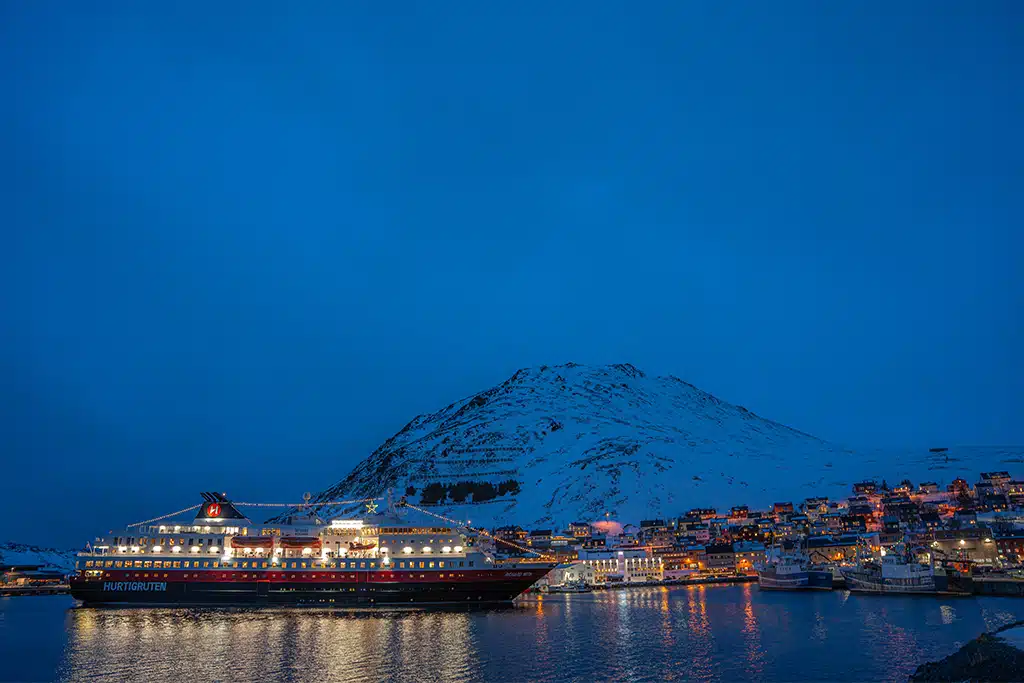 Lichter einer Hafenstadt und eines Schiffes bei Dämmerung in Skandinavien im Winter.