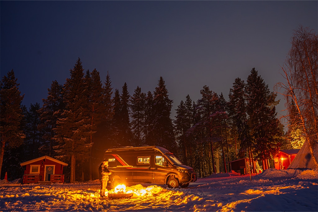 Campervan im Schnee neben einem Feuer beim Wintercamping.