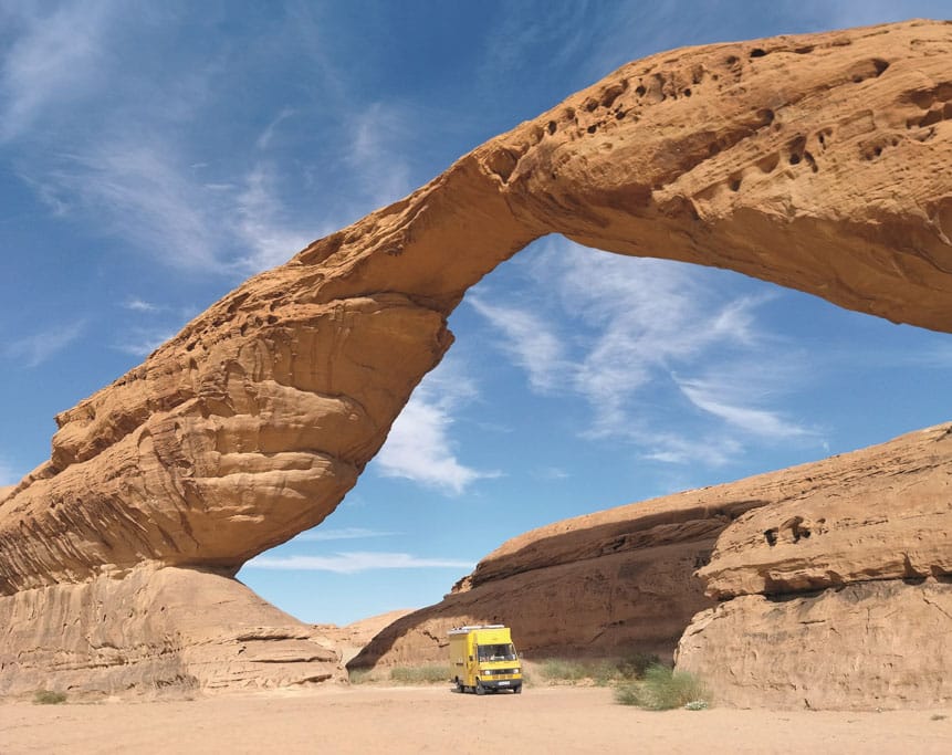 Hoher Sandsteinbogen, unter dem ein gelber Postbus durchfährt