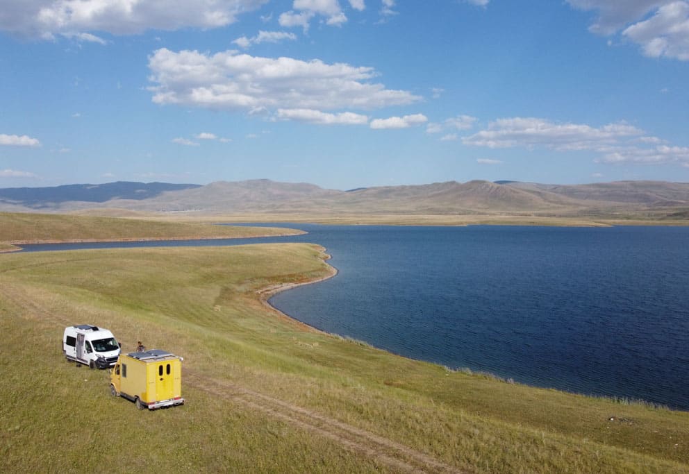 Gelber Postbus und weißes Fahrzeug stehen am Ufer eines großen Sees