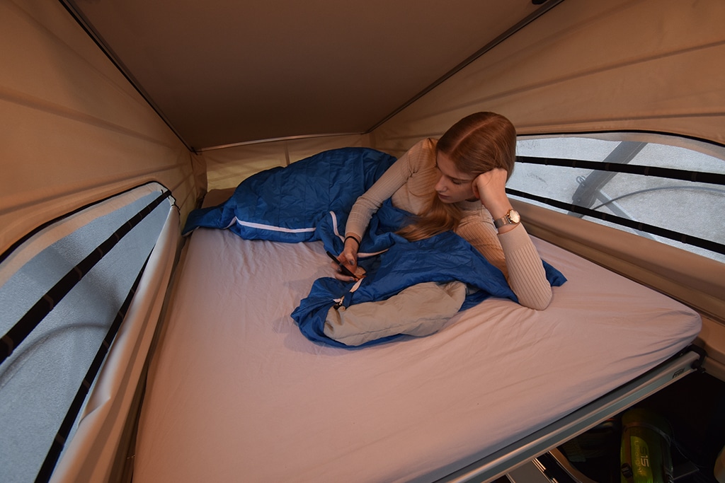 Frau am Handy auf dem Bett des Dachzeltes des Mercedes-Benz Marco Polo.