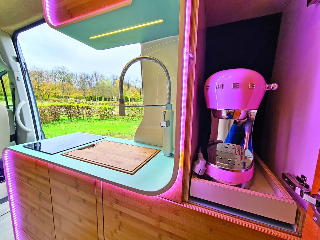 Küchenblock mit großem Schwenkhahn und Abdeckung für die Spüle aus Bambus. Im Schrank rechts daneben eine Espressomaschine im Retro-Look.