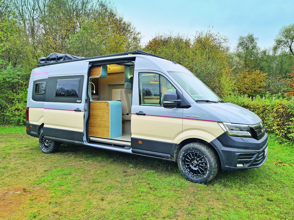 Camper-Schmiede Marylin in beige-grau mit geöffneter Schiebetüre auf Wiese vor Bäumen