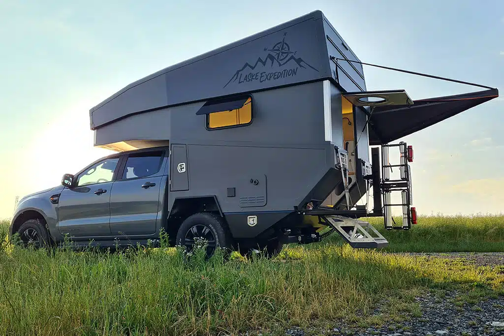 Ein Iveco Daily 4x4 mit einer Wohnkabine mit Parallelhubdach steht auf einer Wiese.