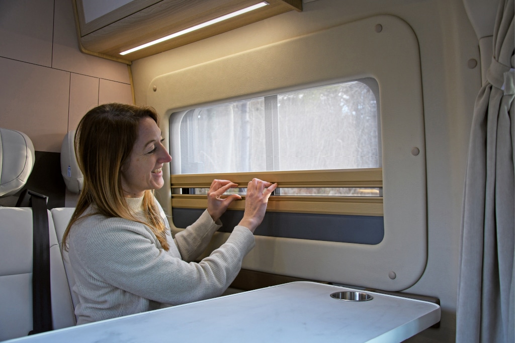 Frau bewegt integrierten Mückenschutz am Fenster am Essplatz