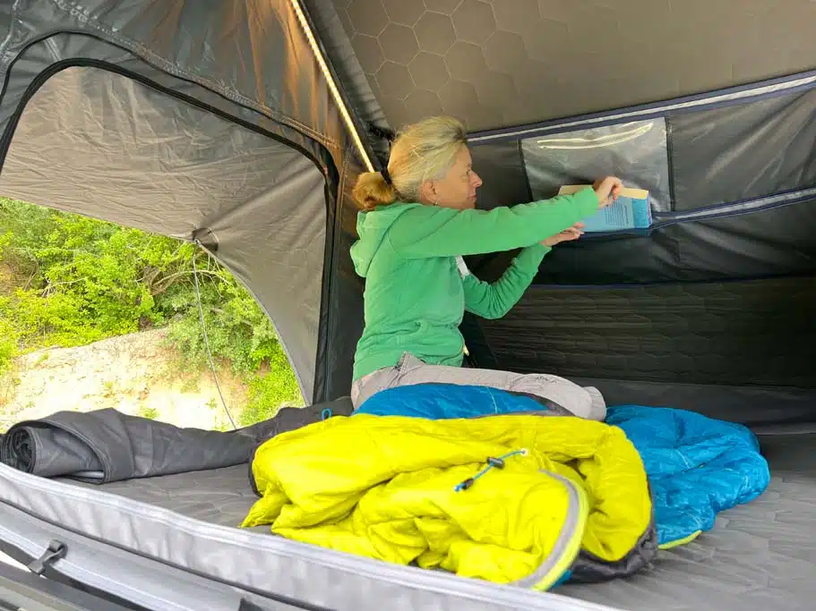 Blick in den Innenraum des Naturbummler Dachzelts Alulight XL, in dem eine Frau gerade ein Buch in einer Tasche verstaut.