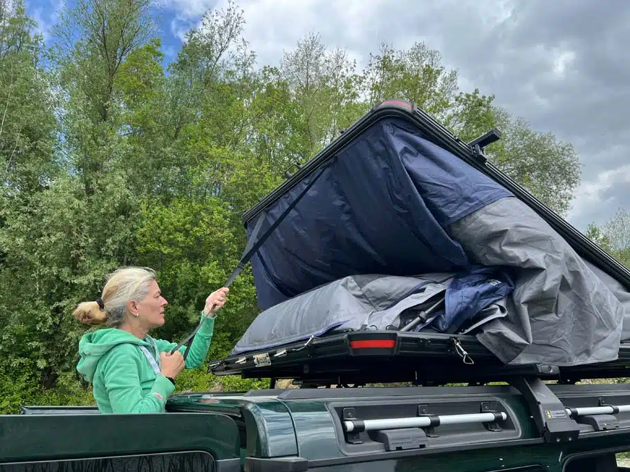 Eine Frau zieht die Dachschale des Naturbummler Dachzelts Alulight XL herunter, um es zu schließen.
