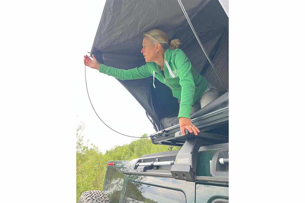 Eine Frau stellt das Vordach des Naturbummler Dachzelts Alulight XL nach vorne aus.