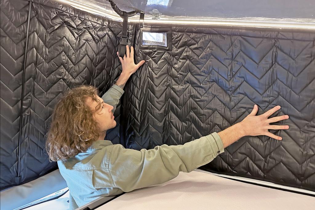 Mann bringt Isoliermatten im Aufstelldach eines Campervans an.