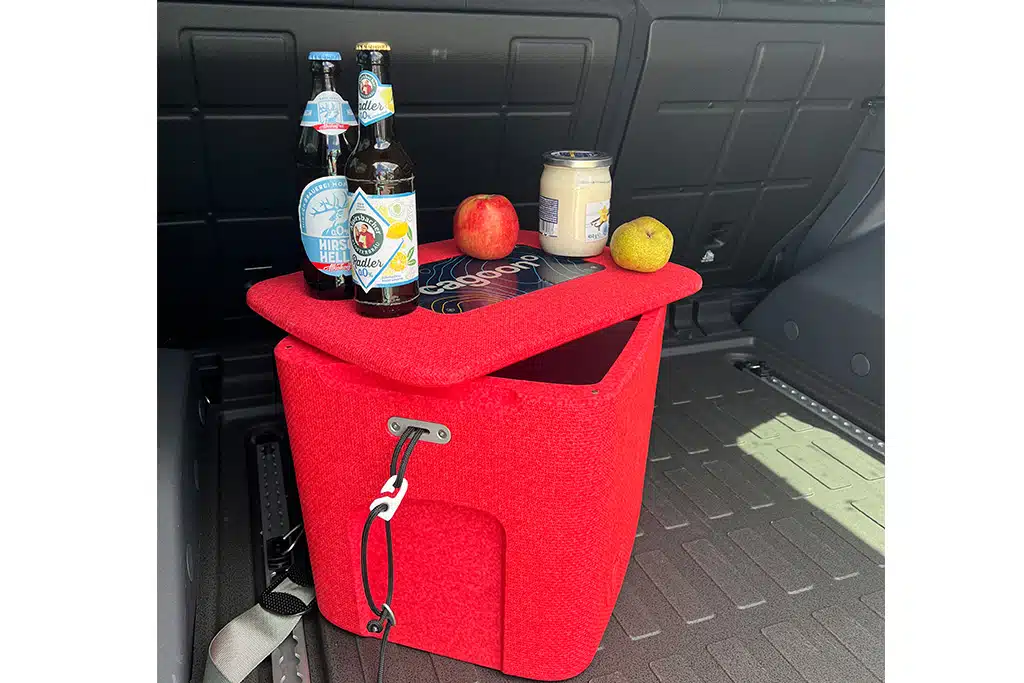 Die Cagoon Passivkühlbox steht im Kofferraum eines Autos, auf ihrem Deckel einige Flaschen und Getränkedosen