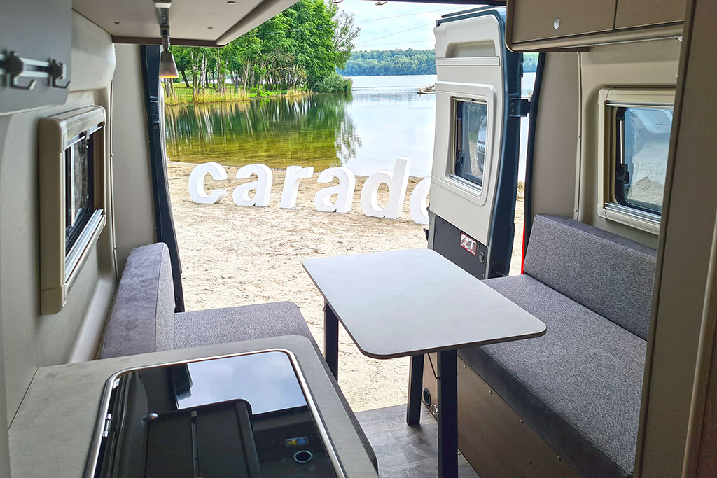 Sitzbänke im Heck und Aussicht auf einen See durch offene Hecktüren eines Campervans