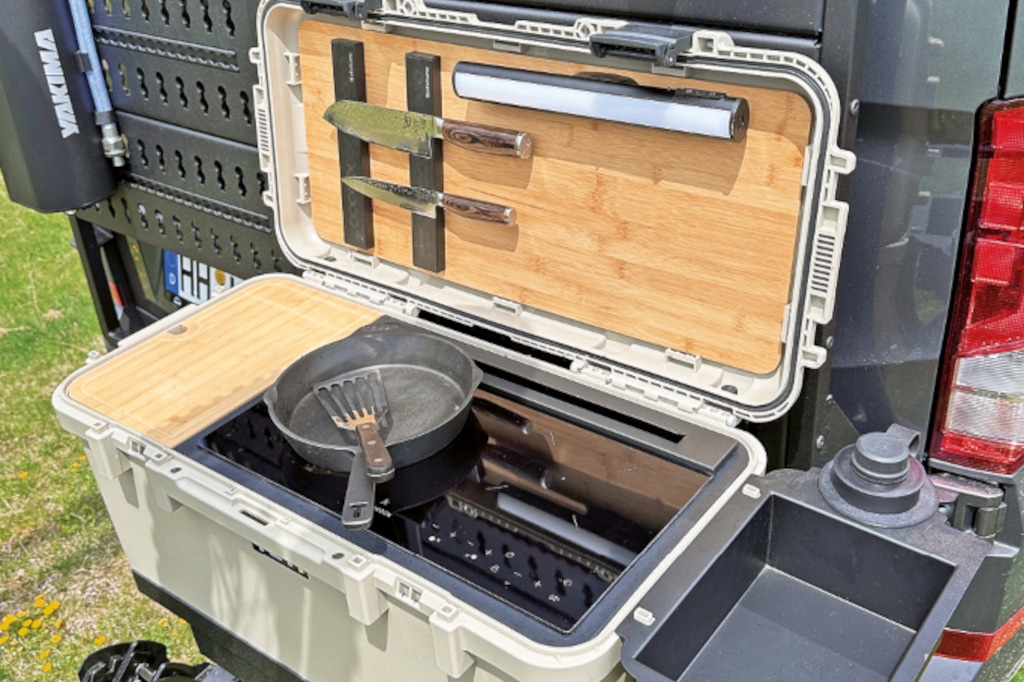 Transportkiste am Heckträger mit offenem Deckel, darin komplette Küche