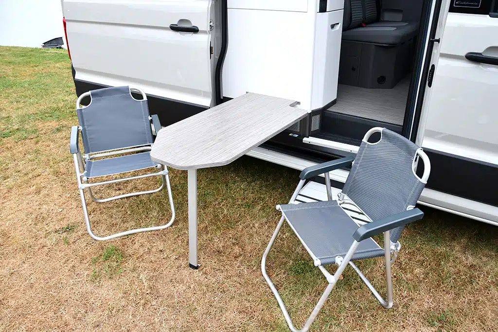 Tisch außen am Küchenblock des Campervans eingehängt, daneben zwei Campingstühle