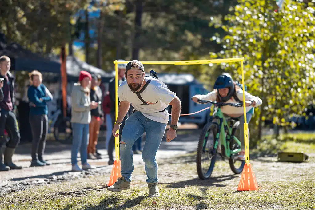 Ein Mann läuft unter einem niedrigen Tor auf einem Parcous durch, dahinter fährt eine Frau auf einem Mountainbike.