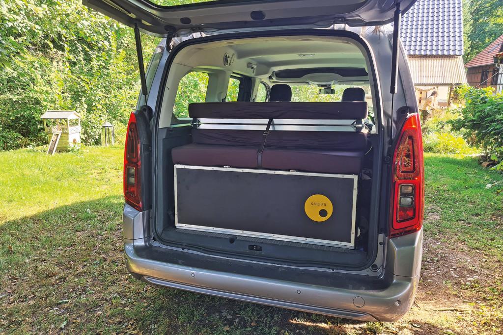 Silberner Hochdachkombi mit geöffneter Heckklappe und eingesetzer Campingbox