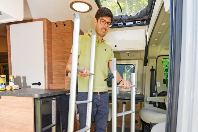 Mann hält zweiteilige Leiter im Innenraum für Aufstieg ins Dachzelt