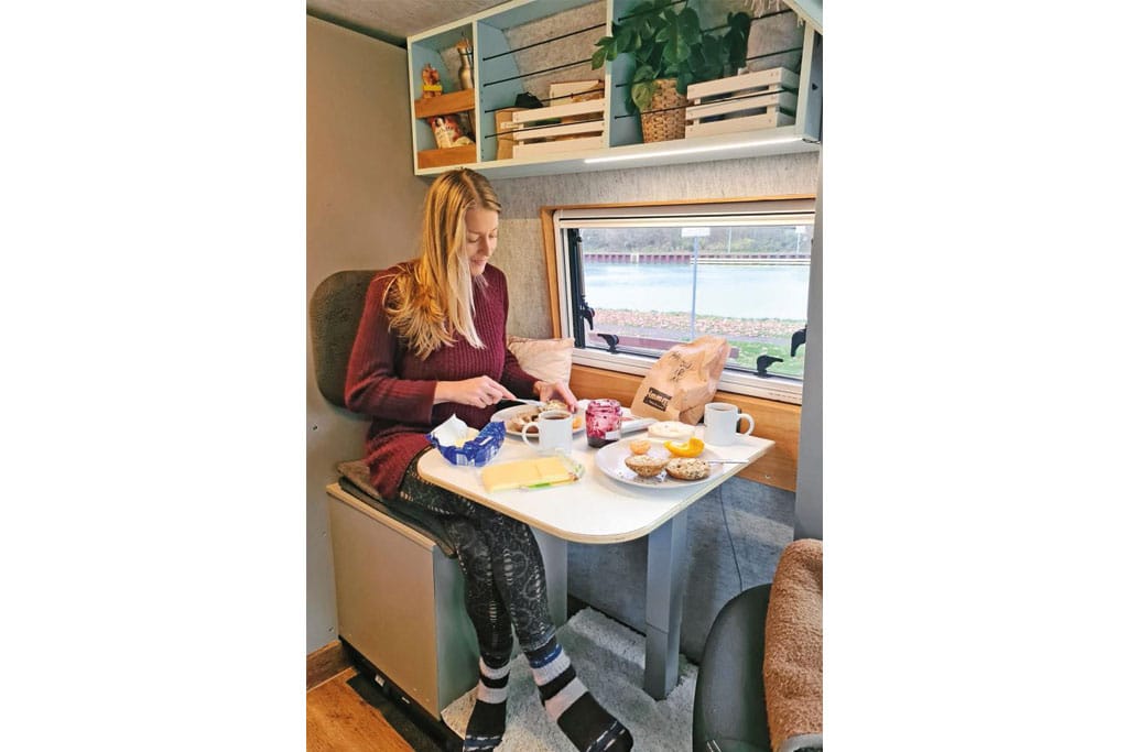 Frau sitzt an kleinem Tisch im Campervan