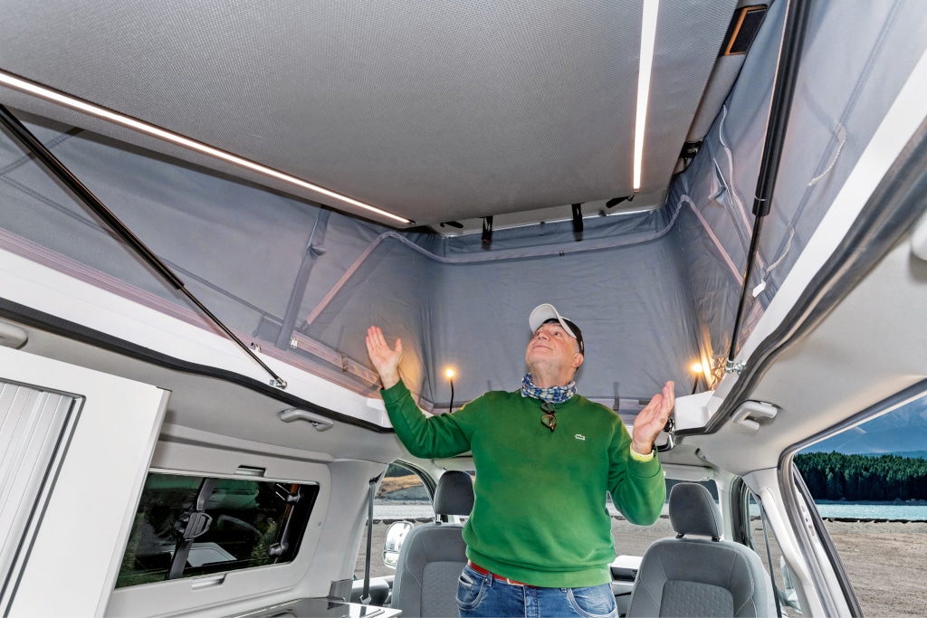 Mann steht im Camper mit hochgestelltem Dach