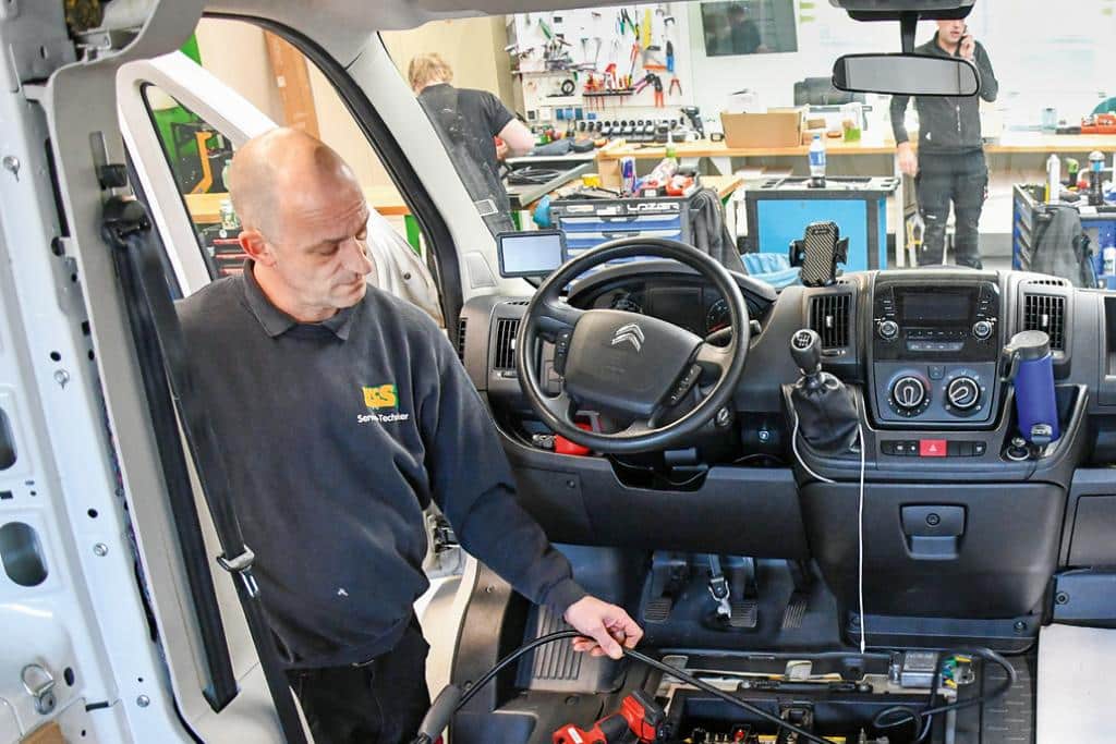 Techniker arbeitet im Fahrerhaus eines Campervans an Kabeln und Fahrzeugelektrik