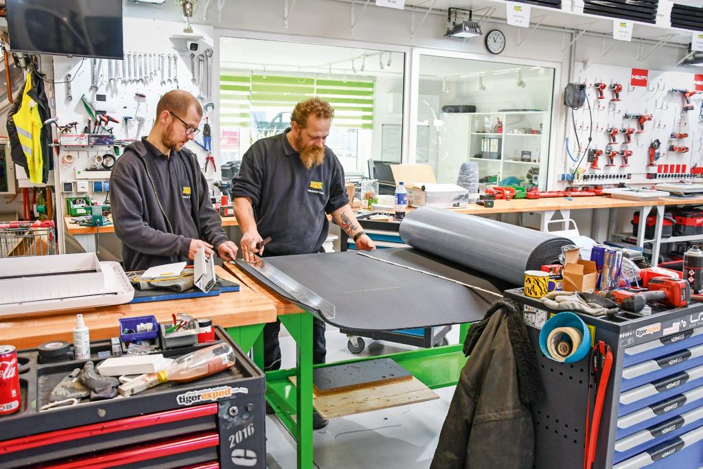Zwei Techniker bearbeiten Dämm- oder Verkleidungsmaterial an einer Werkbank