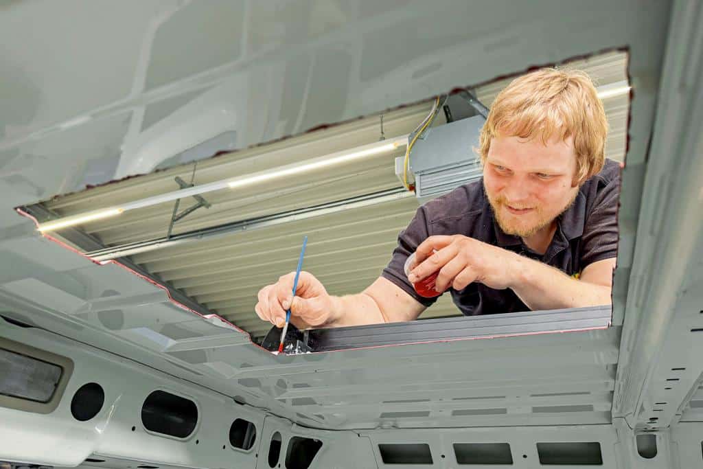 Techniker trägt Dichtmasse an einer Dachöffnung eines Campervans auf