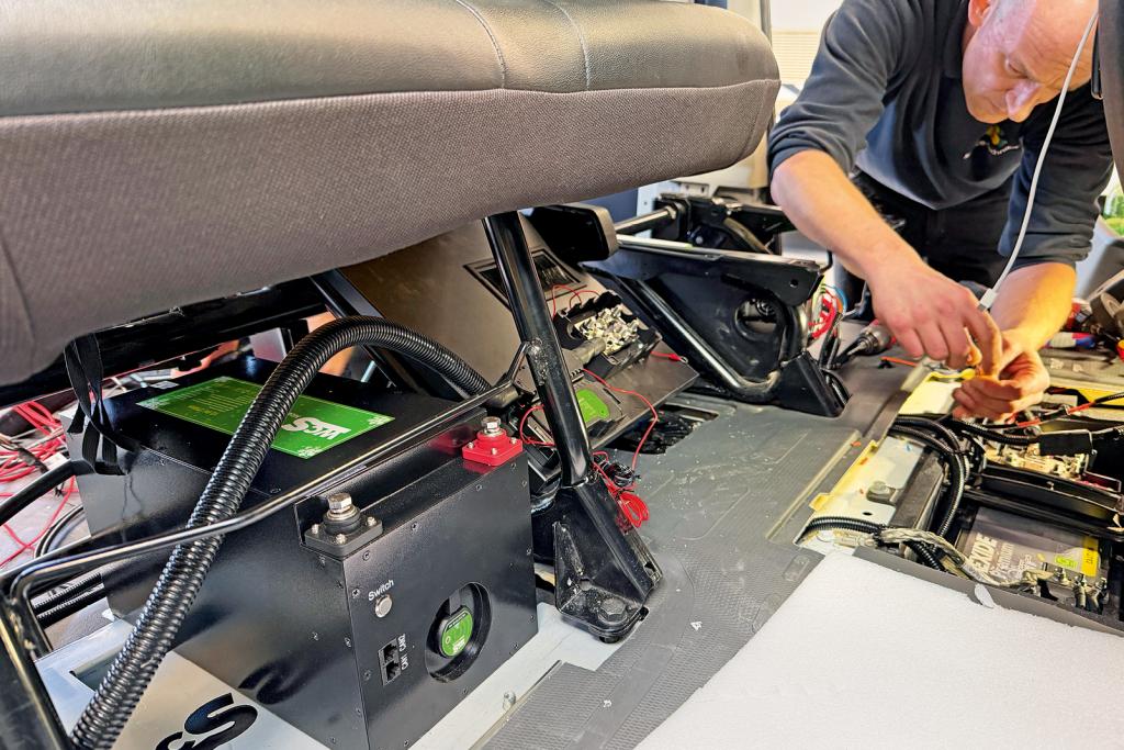 Techniker arbeitet an Kabeln und Elektronik unter einer Sitzbank im Campervan