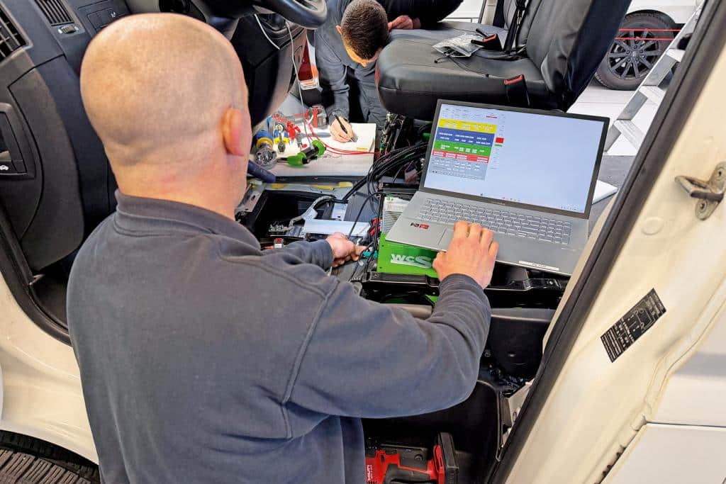 Techniker arbeitet im Fahrerhaus eines Campervans mit Laptop an der Fahrzeugelektrik
